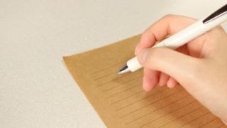 ペンを持ち紙に文字を書いている