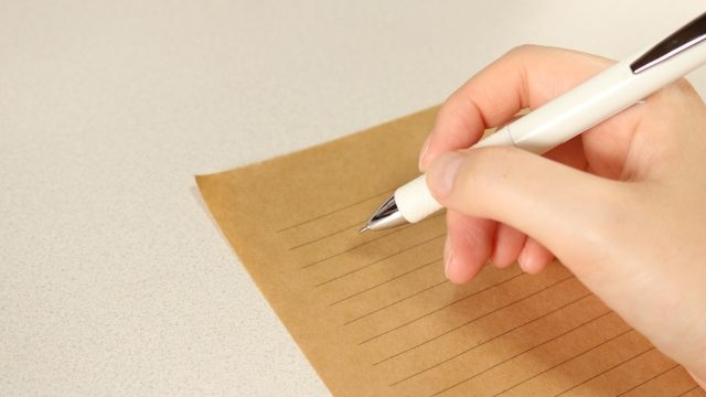 ペンを持ち紙に文字を書いている