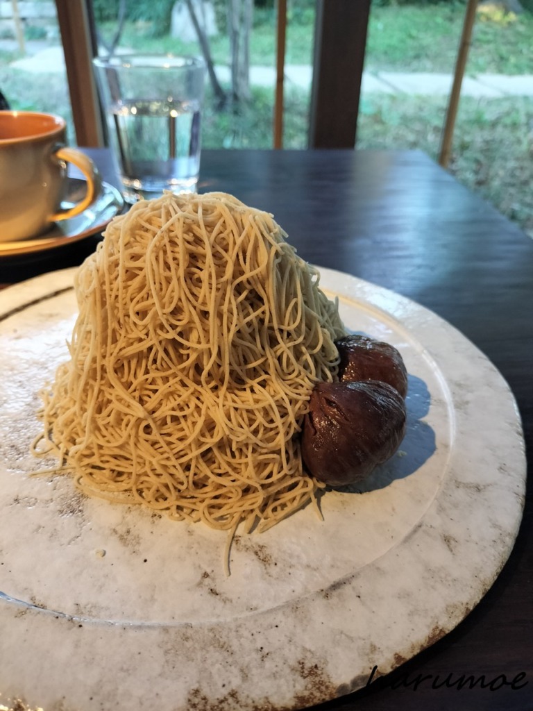 丹波栗のモンブランと渋皮煮。栗ペーストが細く絞られ、山のように盛り付けられたモンブランと、大きな栗の渋皮煮が二つ添えられた、白っぽいお皿に乗った丹波栗しぼりたてモンブラン。
