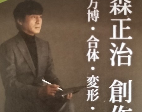 河森正治 創作展のチケット。上部には太陽の塔の顔が写っており、その下に黒いタートルネックとスーツを着た河森正治氏が座っている写真がある。タイトルは「河森正治 創作展 〜万博・合体・変形・未来〜」。